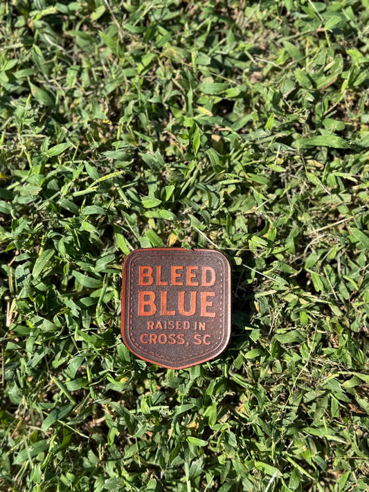 Standalone shield-shaped Bleed Blue leather patch with Raised in Cross, SC lettering.